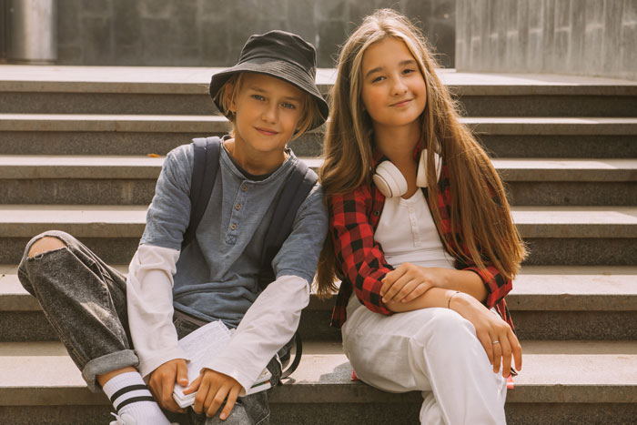 Stepmom’s children sitting on steps, smiling, wearing casual clothes and headphones.