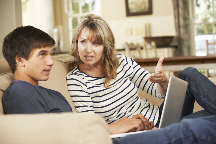 Stepmom having a serious discussion with teenage stepson on the sofa, holding a laptop, in a well-lit living room. Stepmom having a serious discussion with teenage stepson on the sofa, holding a laptop, in a well-lit living room.