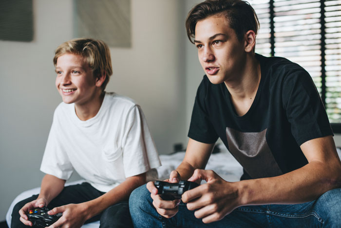 Teenagers playing video games intently indoors, concentrating on their game controllers. Teenagers playing video games intently indoors, concentrating on their game controllers.