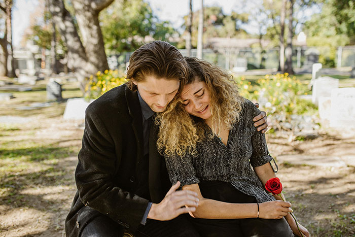 A couple seated in a cemetery, sharing a comforting embrace, symbolizing emotional karma amidst past family turmoil. A couple seated in a cemetery, sharing a comforting embrace, symbolizing emotional karma amidst past family turmoil.