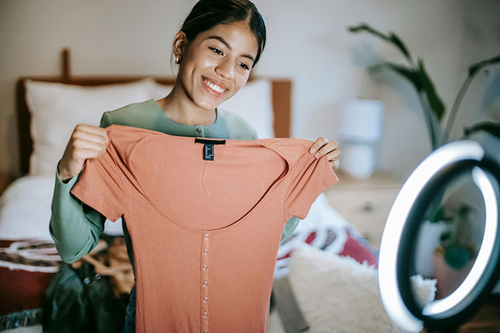 Young woman smiling and holding a dress under a ring light, suggests emotions tied to karma and personal stories. Young woman smiling and holding a dress under a ring light, suggests emotions tied to karma and personal stories.