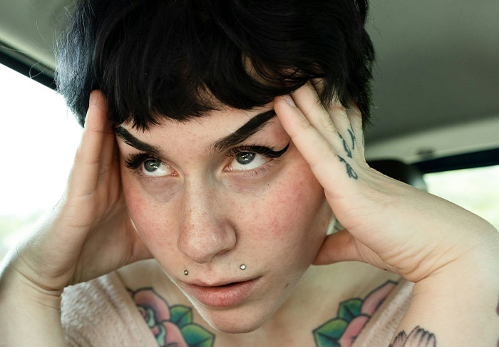 Student looking shocked and distressed in a car, featuring tattoos and piercings. Student looking shocked and distressed in a car, featuring tattoos and piercings.