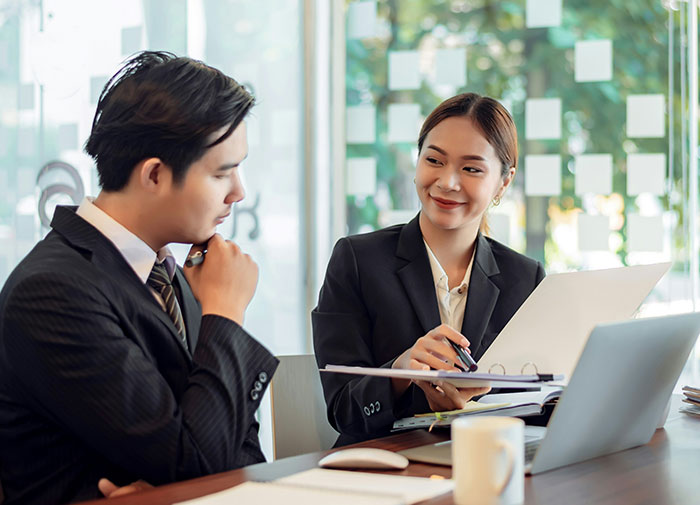 Young professionals in a meeting, discussing documents and using a laptop in a modern office setting. Young professionals in a meeting, discussing documents and using a laptop in a modern office setting.