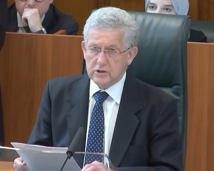 A man in a suit speaking at a podium in a formal setting. A man in a suit speaking at a podium in a formal setting.