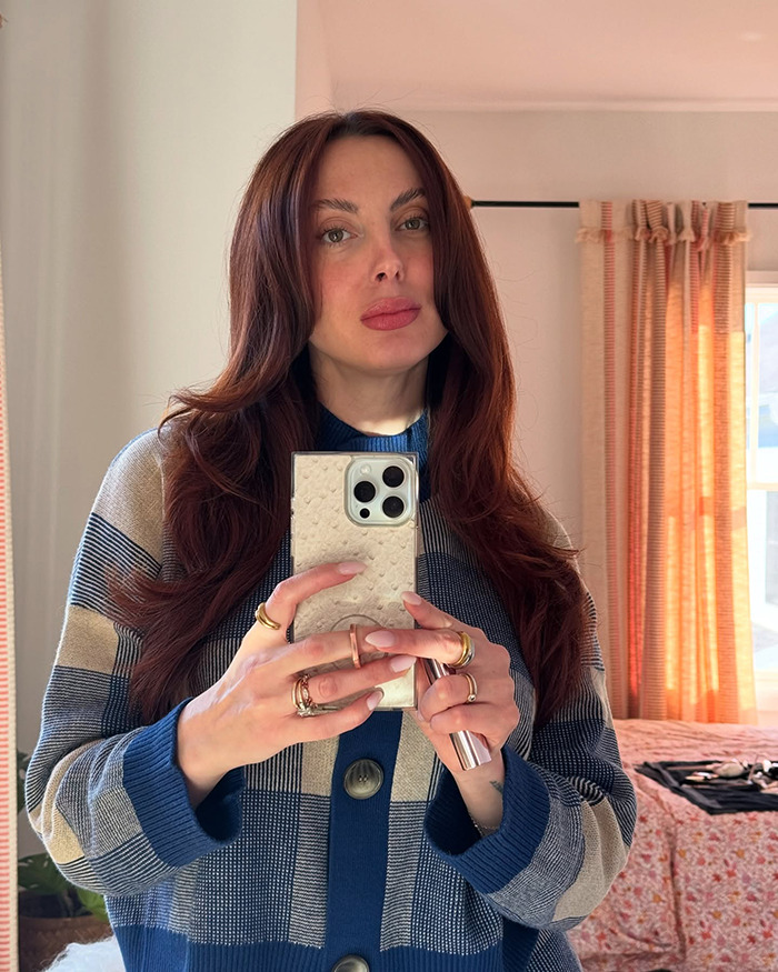 A woman with red hair taking a mirror selfie, wearing a blue and beige striped cardigan. A woman with red hair taking a mirror selfie, wearing a blue and beige striped cardigan.