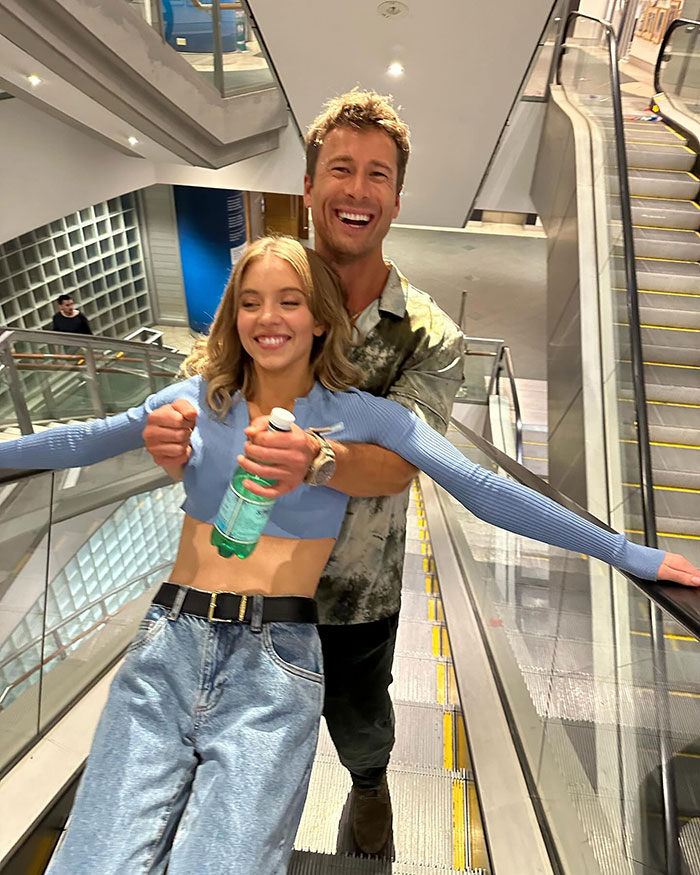 Sydney Sweeney smiling playfully on an escalator, wearing casual attire, causing fan debates about her dress choice. Sydney Sweeney smiling playfully on an escalator, wearing casual attire, causing fan debates about her dress choice.
