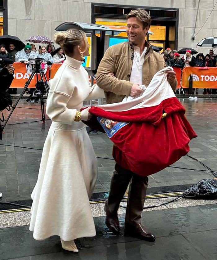 Sydney Sweeney in white dress discusses with man in beige jacket, surrounded by onlookers and camera crew. Sydney Sweeney in white dress discusses with man in beige jacket, surrounded by onlookers and camera crew.