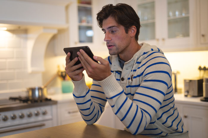 Man in kitchen using tablet, wearing striped sweater, related to engagement pic post issue on Instagram. Man in kitchen using tablet, wearing striped sweater, related to engagement pic post issue on Instagram.