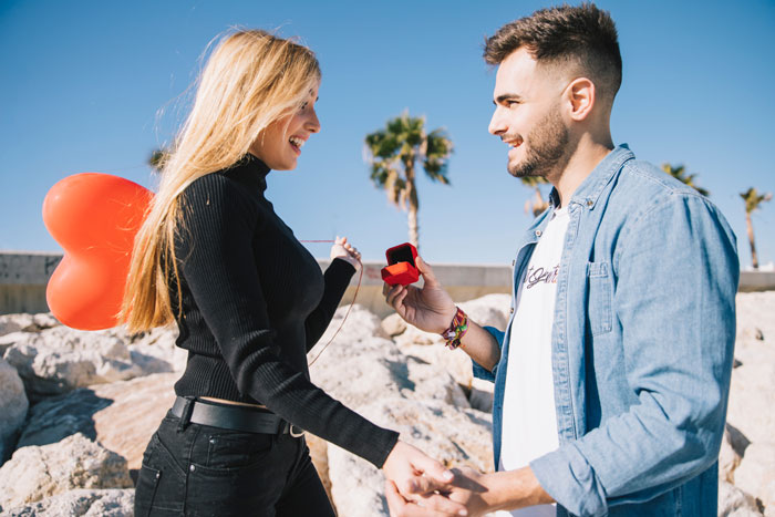 Woman holds heart balloon while man presents engagement ring, symbolizing a joyful proposal moment. Woman holds heart balloon while man presents engagement ring, symbolizing a joyful proposal moment.