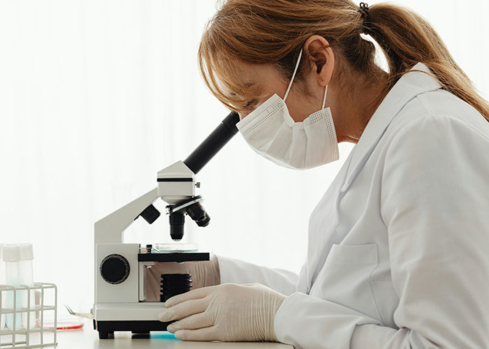 A scientist in a white coat and mask using a microscope for research. A scientist in a white coat and mask using a microscope for research.