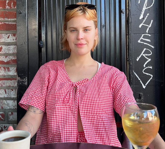 Young woman in red checkered shirt sitting outdoors with coffee and wine, suggesting a comment about Ashton Kutcher. Young woman in red checkered shirt sitting outdoors with coffee and wine, suggesting a comment about Ashton Kutcher.