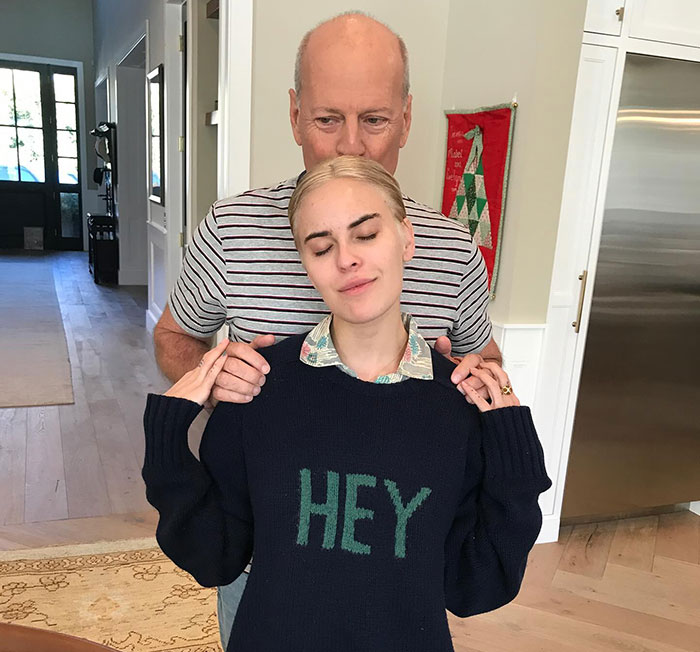 Demi Moore's daughter in a navy sweater with "HEY," standing with eyes closed, someone behind her indoors. Demi Moore's daughter in a navy sweater with "HEY," standing with eyes closed, someone behind her indoors.
