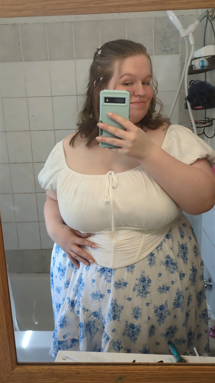 Teen in a floral prom dress taking a mirror selfie in a tiled bathroom. Teen in a floral prom dress taking a mirror selfie in a tiled bathroom.
