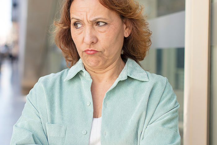 Middle-aged woman with crossed arms looking displeased, illustrating aunt starts drama in niece’s life concept. Middle-aged woman with crossed arms looking displeased, illustrating aunt starts drama in niece’s life concept.
