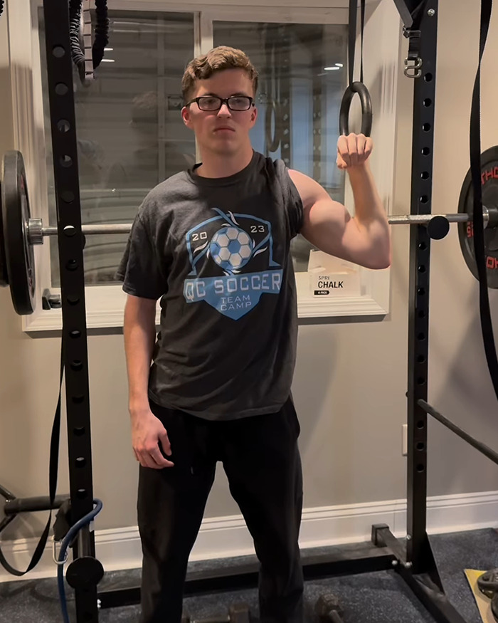 Young man in glasses showcasing his right arm's muscle development, standing near workout equipment, "The Crooked Man. Young man in glasses showcasing his right arm's muscle development, standing near workout equipment, "The Crooked Man.