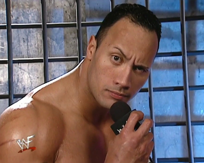 Dwayne Johnson in classic wrestling setting holding a microphone, sparking new movie race confusion. Dwayne Johnson in classic wrestling setting holding a microphone, sparking new movie race confusion.