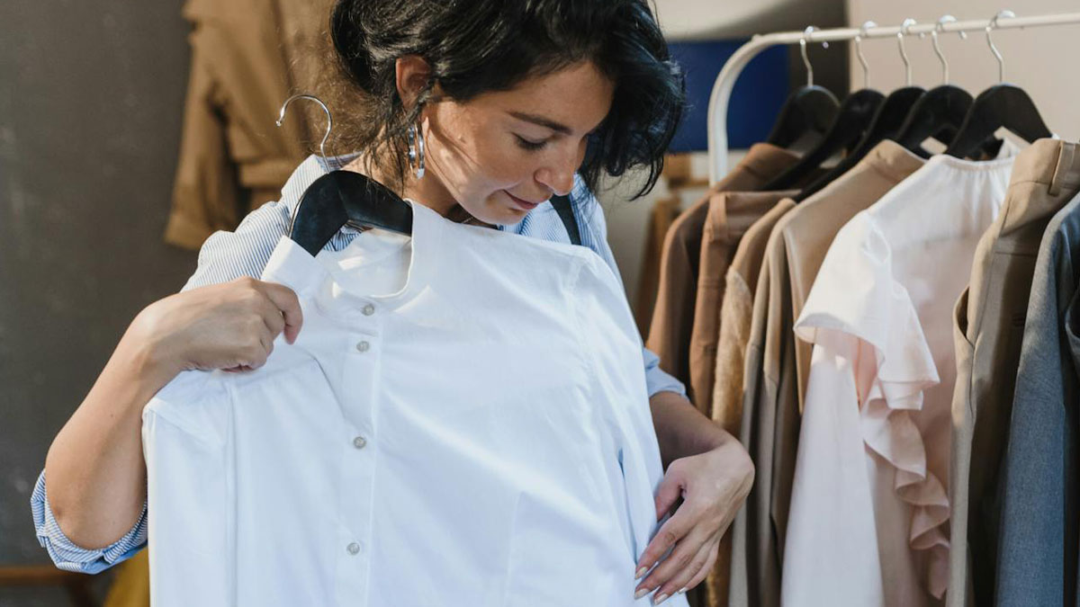 Woman holding a white shirt on a hanger in a clothing store, unrelated to restaurant food or price changes.
