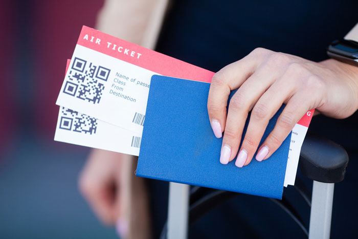 Hand holding an affordable flights ticket and blue passport, resting on a suitcase handle. Hand holding an affordable flights ticket and blue passport, resting on a suitcase handle.