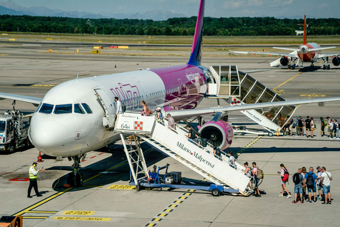 Passengers boarding an affordable flight at an airport via a jet bridge, with an airline crew member assisting. Passengers boarding an affordable flight at an airport via a jet bridge, with an airline crew member assisting.
