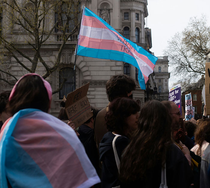 Protest with trans pride flag, people holding signs, highlighting school suspension transphobia issue. Protest with trans pride flag, people holding signs, highlighting school suspension transphobia issue.