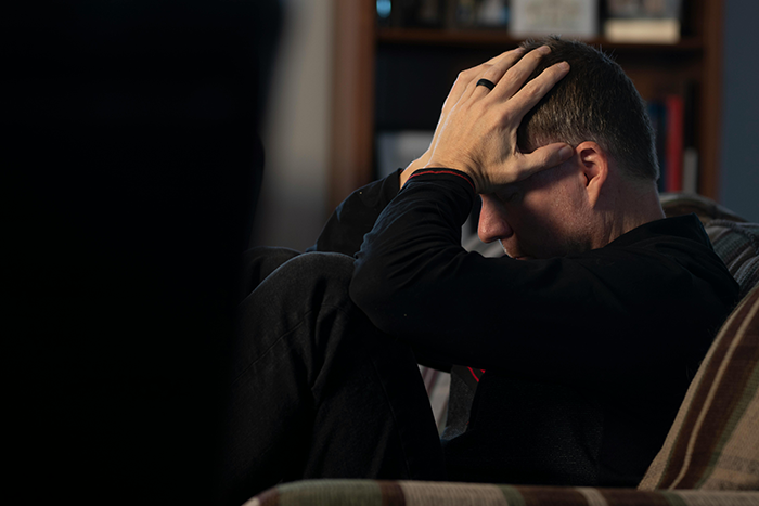 Man sitting on a couch with his head in his hands, appearing stressed and unsure about a wife coming out as trans. Man sitting on a couch with his head in his hands, appearing stressed and unsure about a wife coming out as trans.