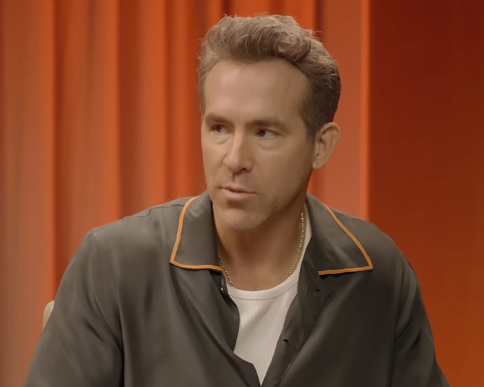 Ryan Reynolds in a casual shirt against an orange backdrop, relevant to Travis Kelce unfollow story. Ryan Reynolds in a casual shirt against an orange backdrop, relevant to Travis Kelce unfollow story.