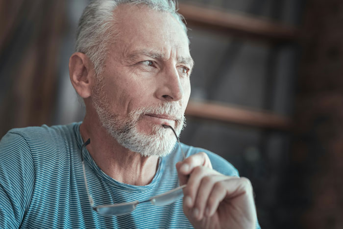 Elderly man in striped shirt holding glasses, deep in thought about family dynamics and LGBT identity. Elderly man in striped shirt holding glasses, deep in thought about family dynamics and LGBT identity.