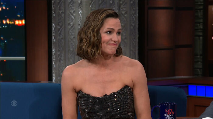 Celebrity in a sparkling dress on a talk show set, smiling warmly.