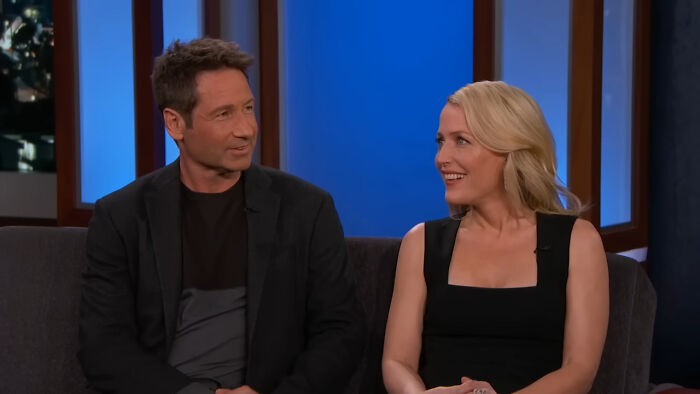 Two celebrities seated on a talk show, smiling and engaging in conversation.