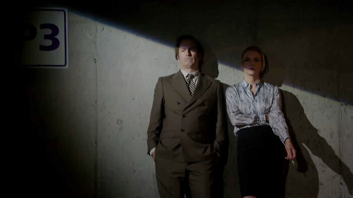 Two people in formal attire leaning against a wall, partially illuminated by light, representing a top-rated show.
