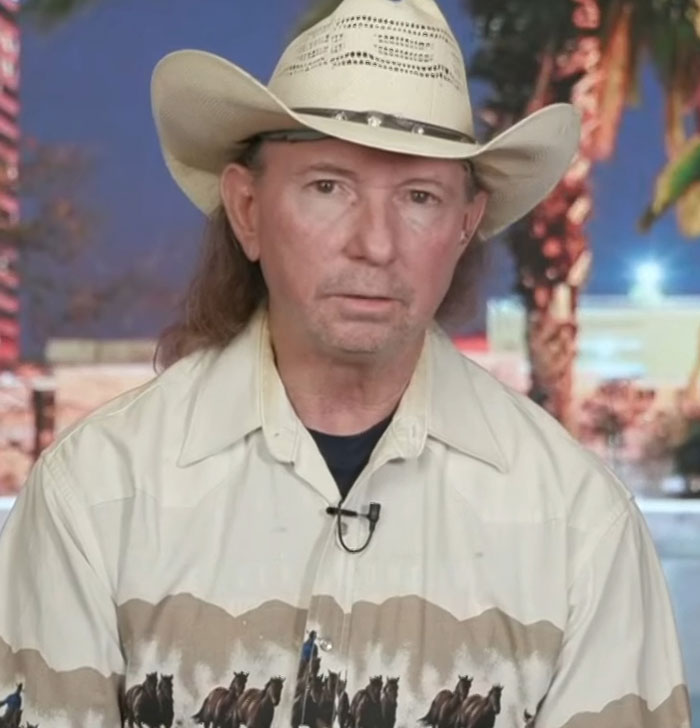 Cowboy in patterned shirt and hat, serious expression, indoor setting with palm decor. Cowboy in patterned shirt and hat, serious expression, indoor setting with palm decor.