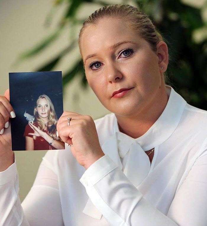 Woman holding a photo, linked to Prince Andrew in legal case, looking serious while seated indoors. Woman holding a photo, linked to Prince Andrew in legal case, looking serious while seated indoors.