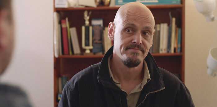 Man with a goatee in a room with a bookshelf, discussing a show maintaining 10/10 quality.