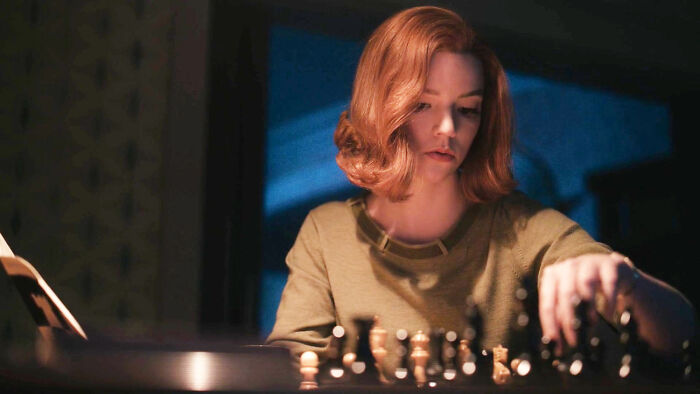 Woman playing chess intently, illuminated under soft light, representing top-rated show vibes.