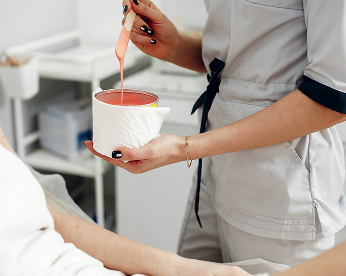 Woman preparing wax in a salon, holding a pink wax jar and applicator, highlighting waxing services. Woman preparing wax in a salon, holding a pink wax jar and applicator, highlighting waxing services.