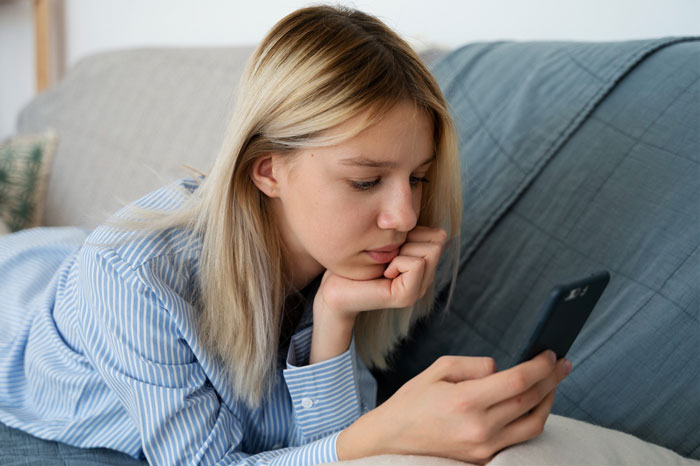 Teen upset after babysitting dispute, looking at her phone while resting on a couch.
