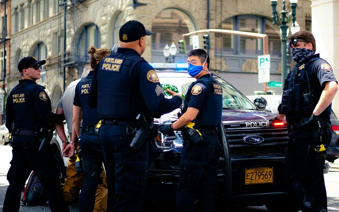 Police officers in Portland gathered around patrol car, highlighting unique American aspects.