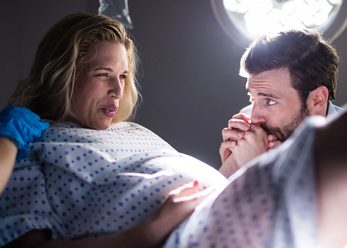 Pregnant woman in hospital gown with partner who appears concerned, highlighting couple dynamics during pregnancy. Pregnant woman in hospital gown with partner who appears concerned, highlighting couple dynamics during pregnancy.