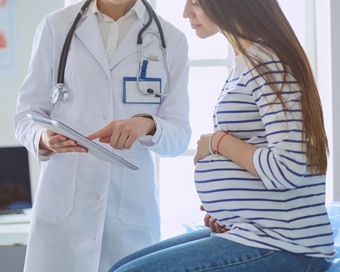 Pregnant woman consulting with a doctor, holding a tablet, wearing a white coat. Pregnant woman consulting with a doctor, holding a tablet, wearing a white coat.