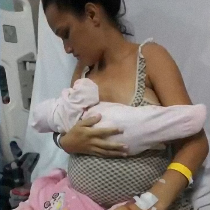 Pregnant woman holding one baby in hospital bed, wearing a patterned dress and yellow wristband. Pregnant woman holding one baby in hospital bed, wearing a patterned dress and yellow wristband.