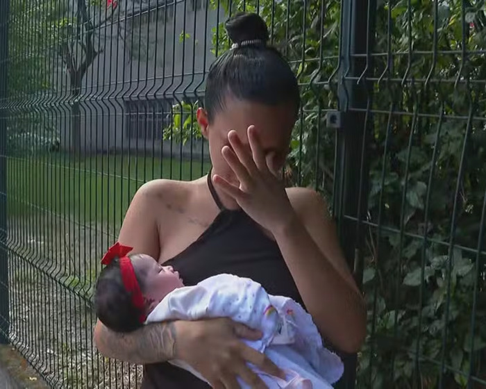 A pregnant woman holds one baby, looking emotional, near a fence. A pregnant woman holds one baby, looking emotional, near a fence.