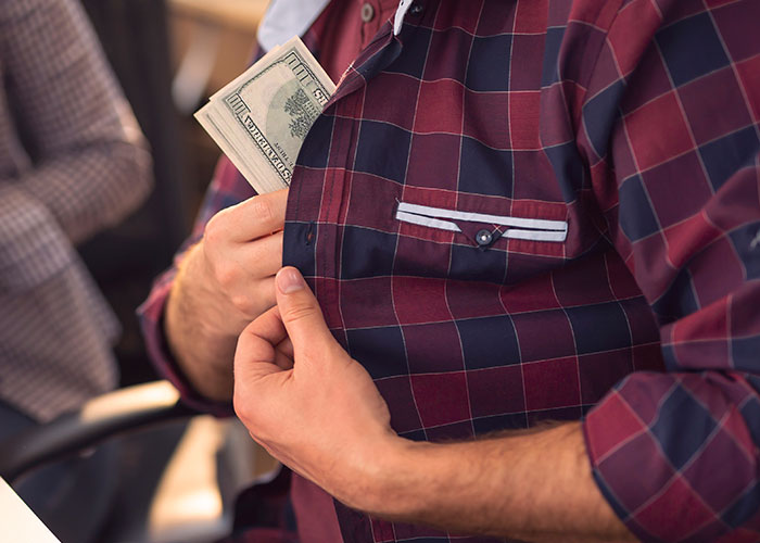Man in a plaid shirt slipping cash into his shirt pocket, related to secretive rent money activity. Man in a plaid shirt slipping cash into his shirt pocket, related to secretive rent money activity.