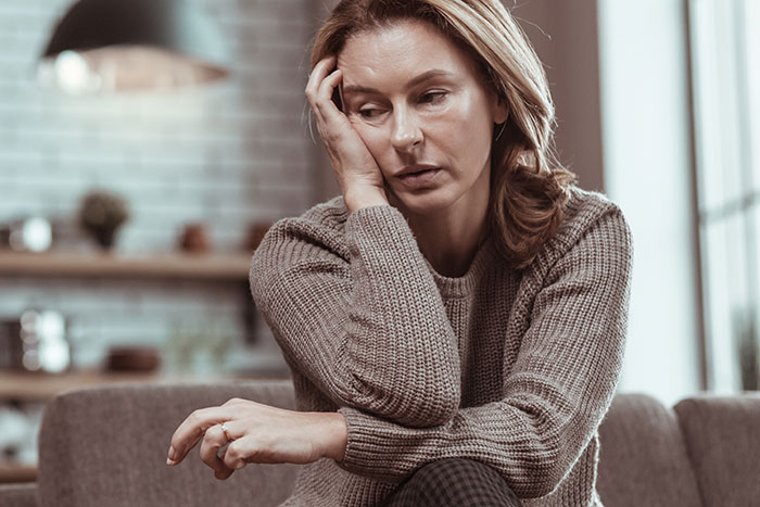 Woman looking pensive, sitting with her hand on her face, in a living room setting. Woman looking pensive, sitting with her hand on her face, in a living room setting.