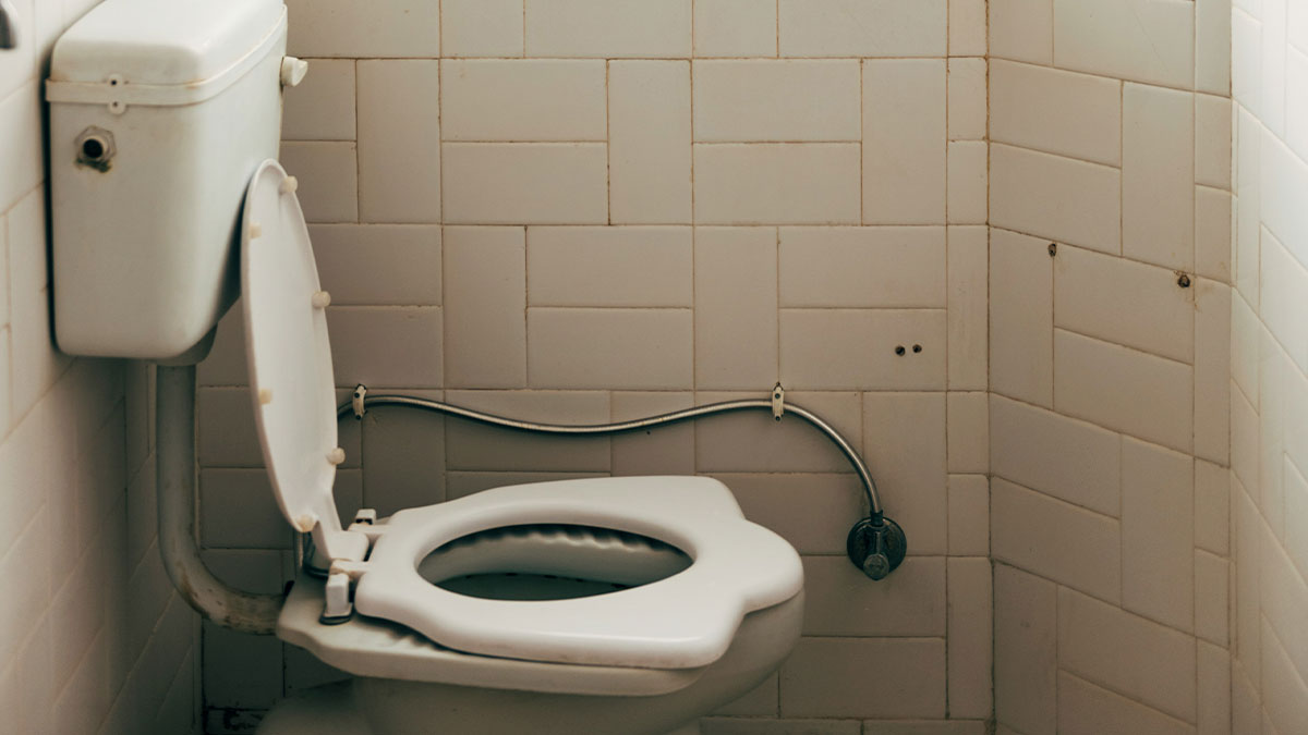 Old toilet with open seat in a small bathroom, highlighting woman noticing new BF doesnu2019t clean toilet after use issue