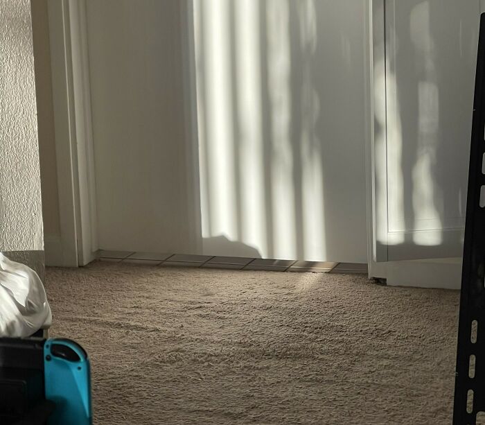 Sunlight casts shadows on a white door and beige carpet, creating a pattern often unnoticed by Americans.