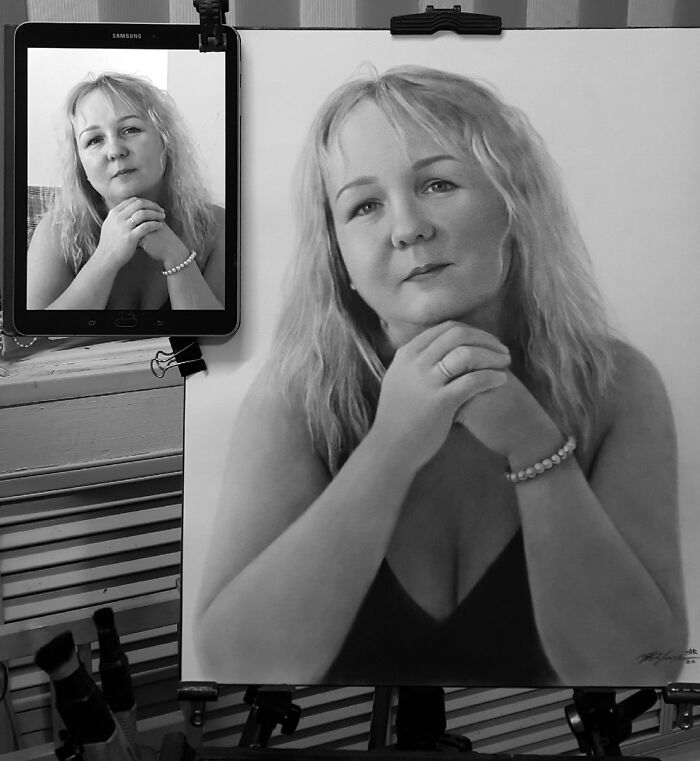 Hyper-realistic pencil portrait of a woman beside a tablet showing her photo.
