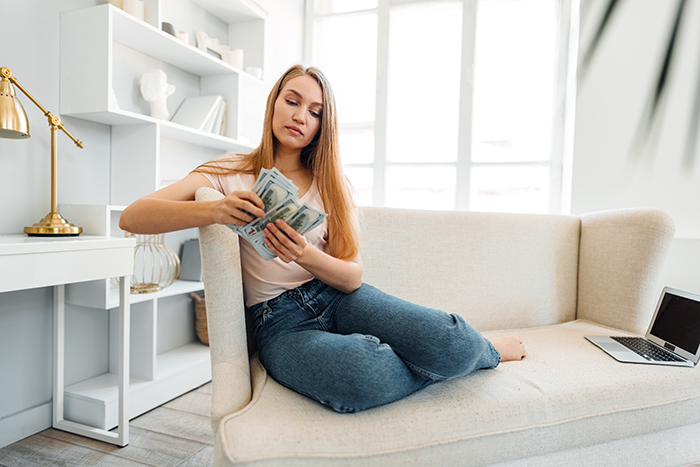 Woman counting money on a couch in a bright room, representing life insurance policy and car refinancing conflict. Woman counting money on a couch in a bright room, representing life insurance policy and car refinancing conflict.