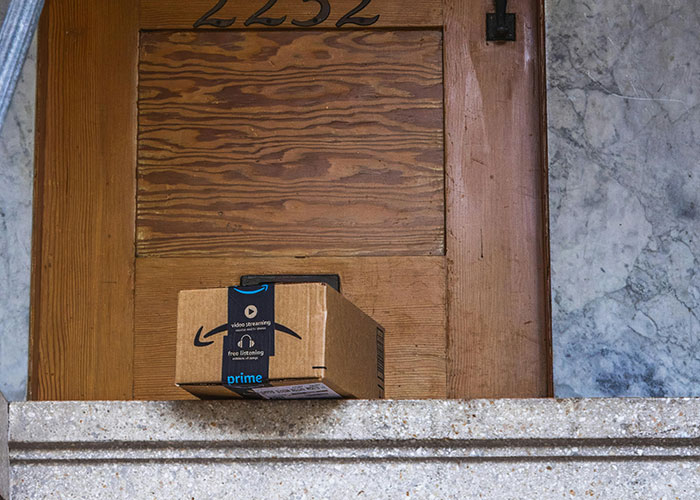 Amazon package left on doorstep outside wooden door, illustrating package stealing and petty neighbor actions. Amazon package left on doorstep outside wooden door, illustrating package stealing and petty neighbor actions.