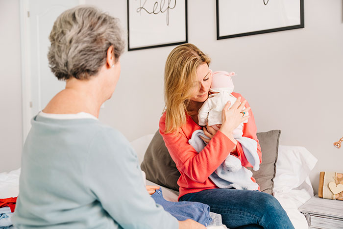 New mom holding her baby while interacting with her mother-in-law in a home setting. New mom holding her baby while interacting with her mother-in-law in a home setting.