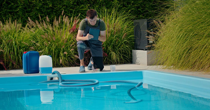 Man inspecting pool equipment with tablet beside a residential pool amid neighbors sending relatives without consent Man inspecting pool equipment with tablet beside a residential pool amid neighbors sending relatives without consent
